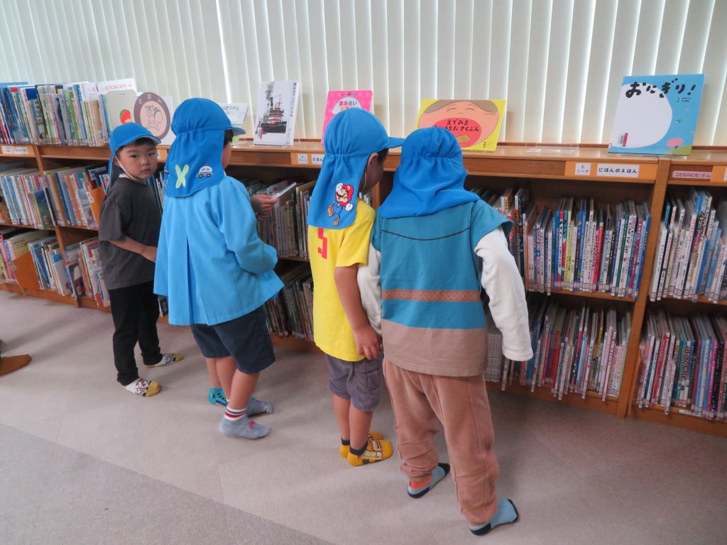 子供たちが図書館の本棚の前で本を見ている様子。