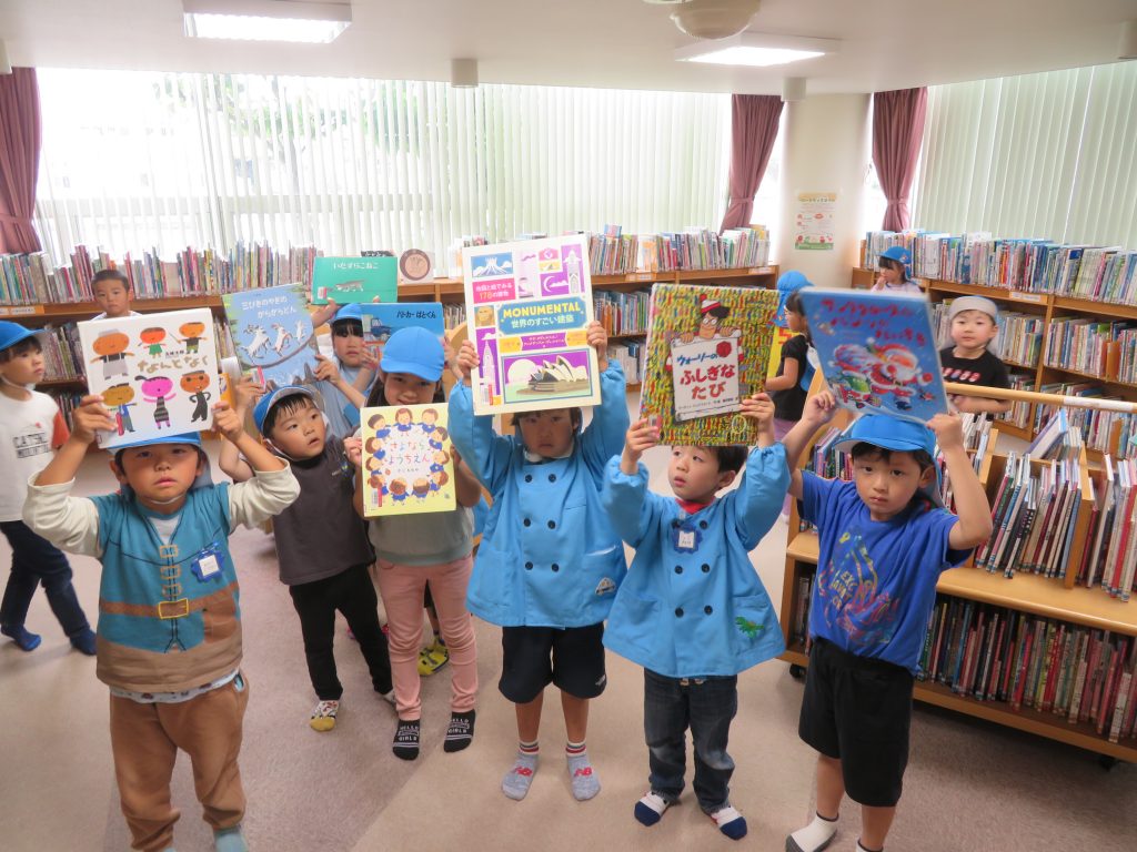 子供たちが本を持って笑顔でポーズをとっている図書館の内部の写真。
