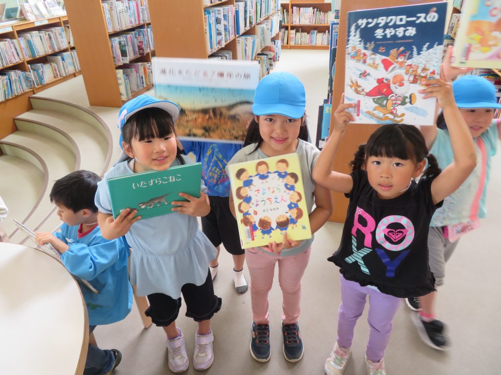 子供たちが図書館で本を持って笑顔でポーズをとっている様子。