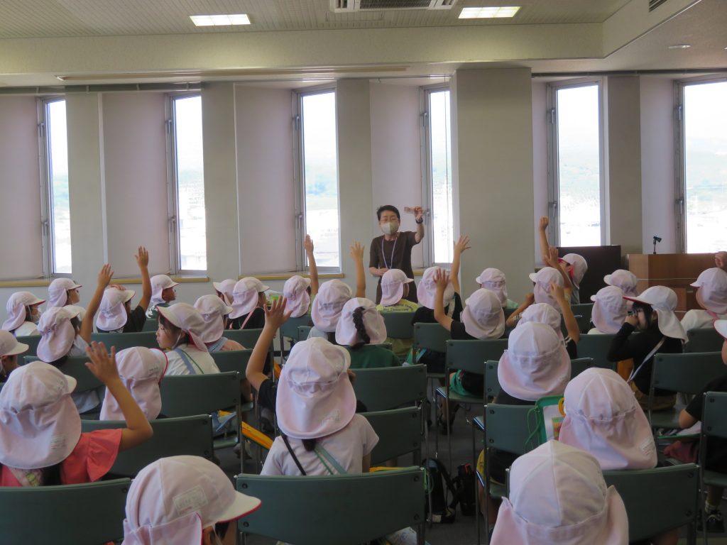 教室で手を挙げる子どもたちと前で指導する大人の姿。