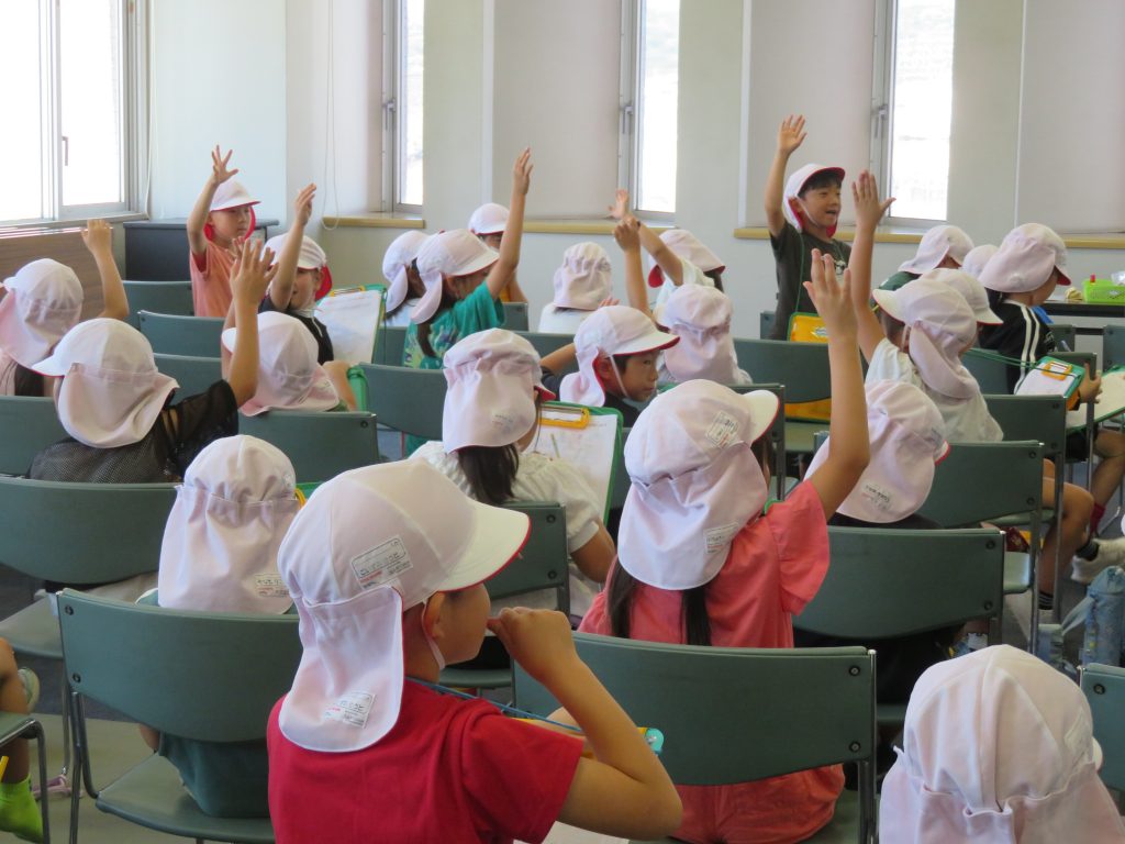 教室で帽子をかぶった子供たちが手を挙げている様子の画像