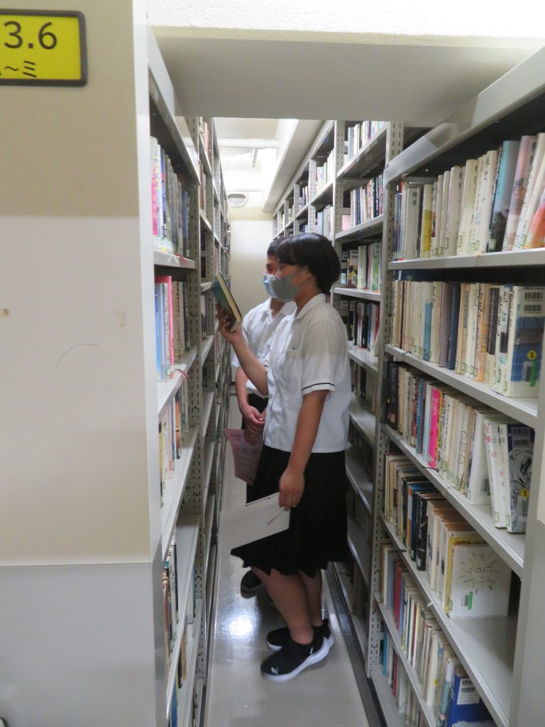 図書館の本棚の間に立っている二人の学生が本を見ている様子