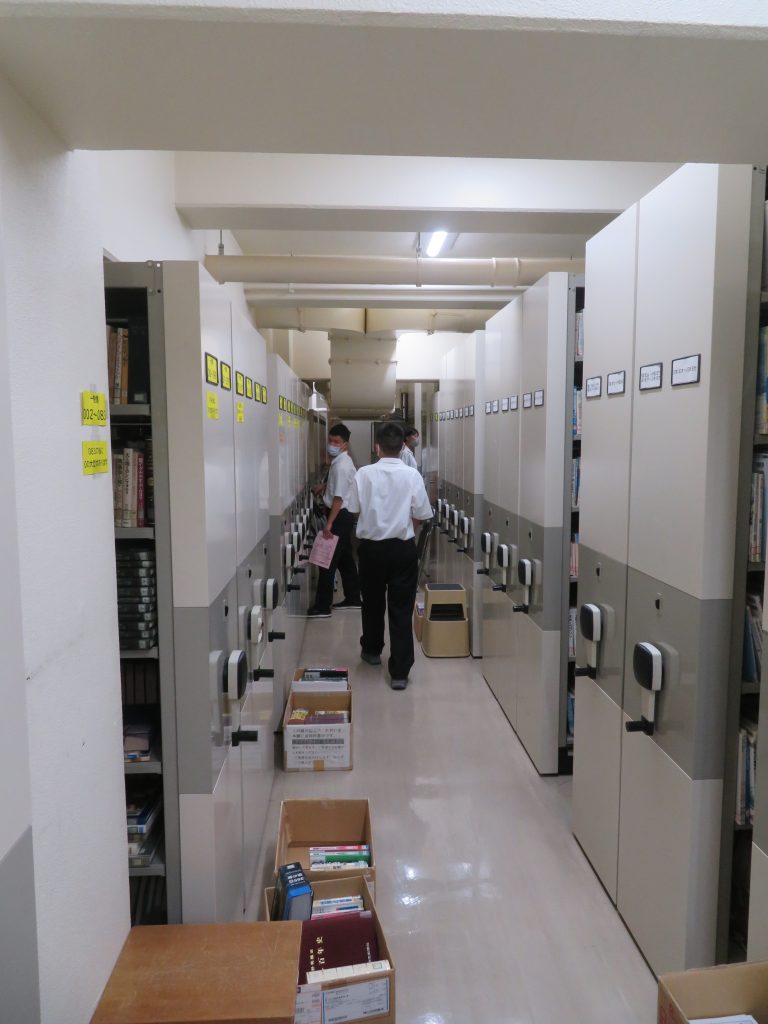 収納棚が並ぶ廊下で作業をしている二人の人物が写っている画像