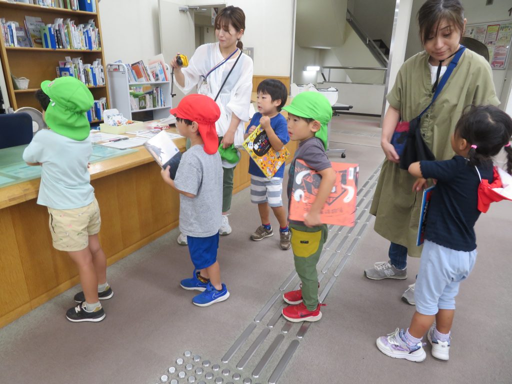 子供たちがカラフルな帽子をかぶり、図書館のカウンターの前で並んでいる様子。