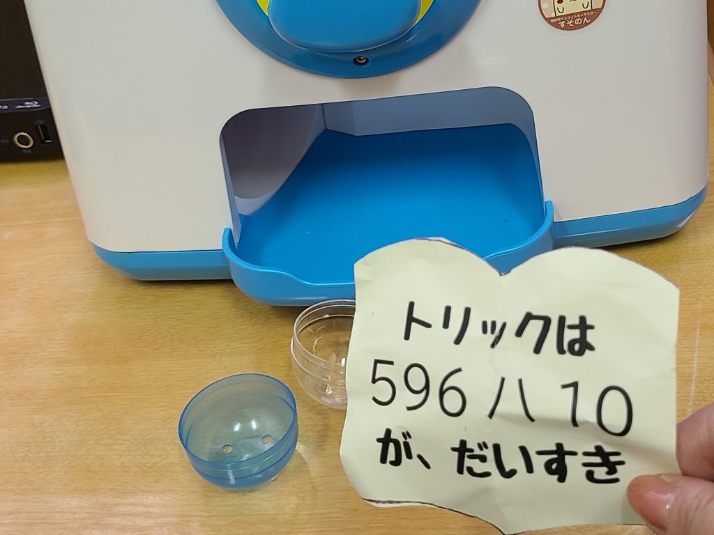 青と白の機械の前に「トリックは596八10が、だいすき」と書かれたメモと透明なカップが置かれている画像。