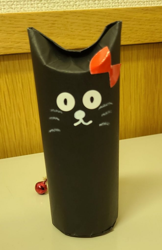 黒い猫の顔が描かれたペン立てで赤いリボンが付いている。