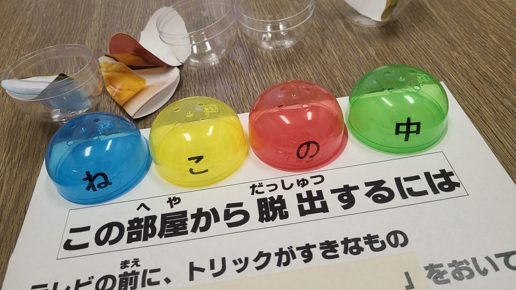 青、黄色、赤、緑のカラフルな丸いオブジェクトと日本語のテキストが書かれた紙が置かれたテーブルの画像。