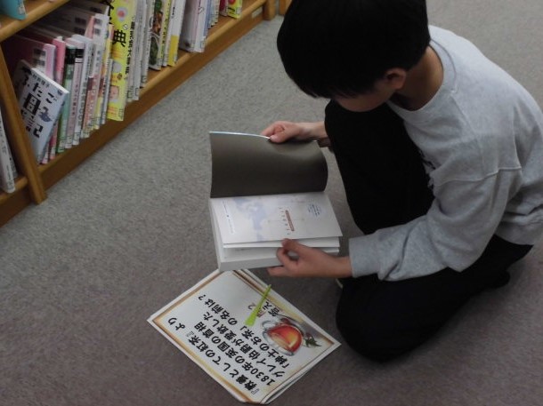 本を手に持ち、床に置かれたチラシを見ている子供の姿