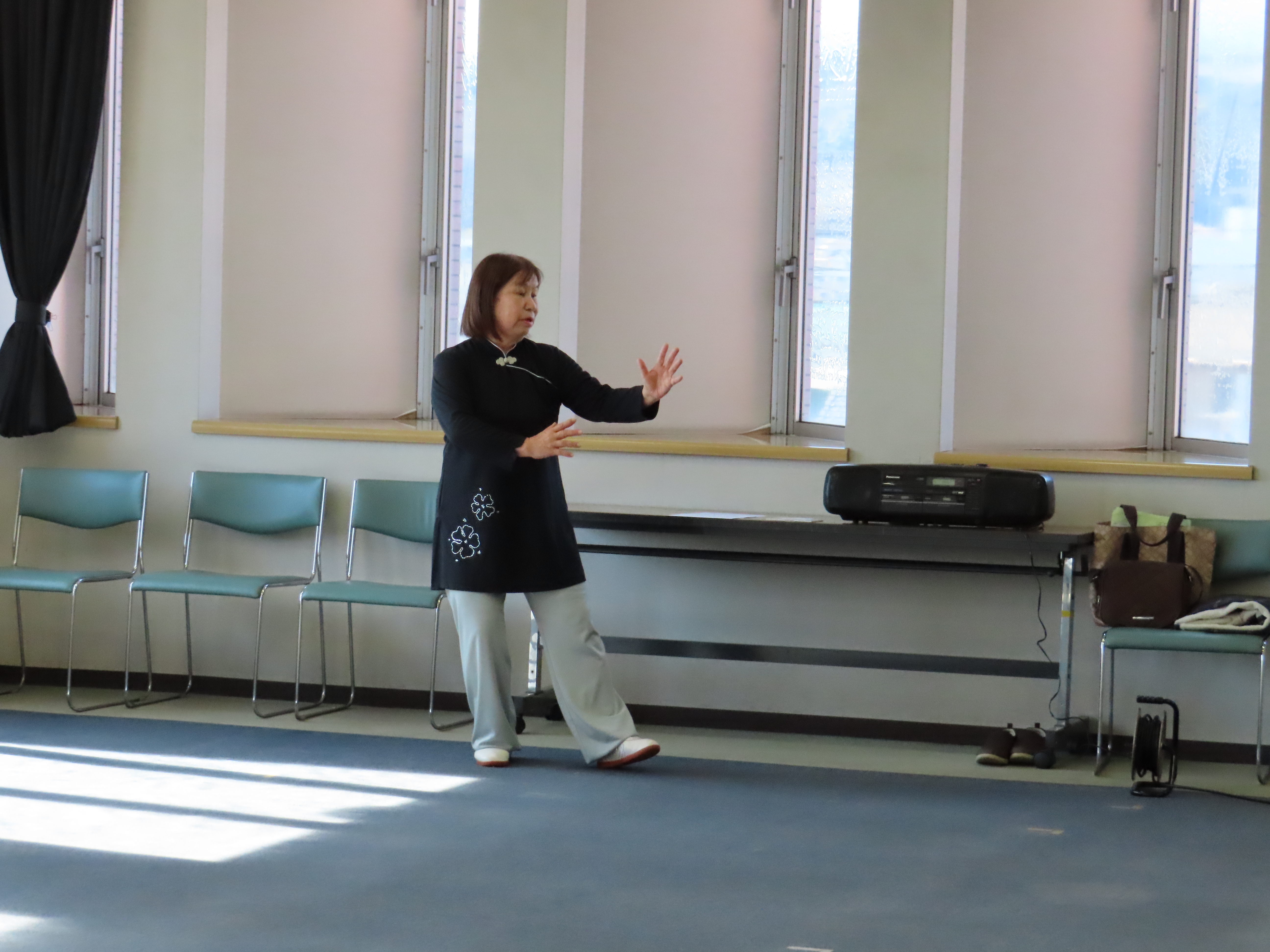 室内の窓際で片手を前に伸ばして太極拳の動作をしている先生