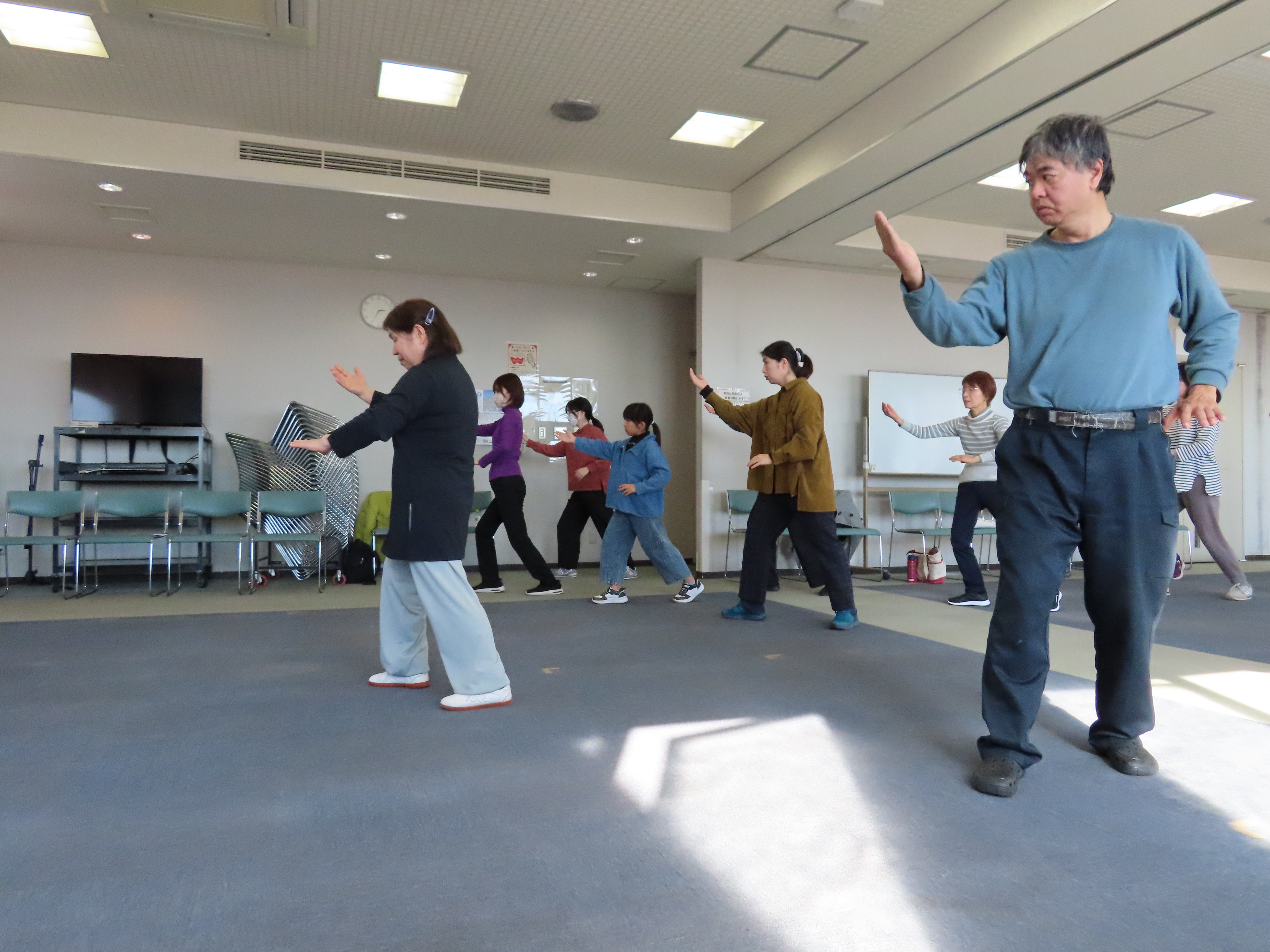 室内の広い会場で複数の人々が揃って太極拳をしている様子