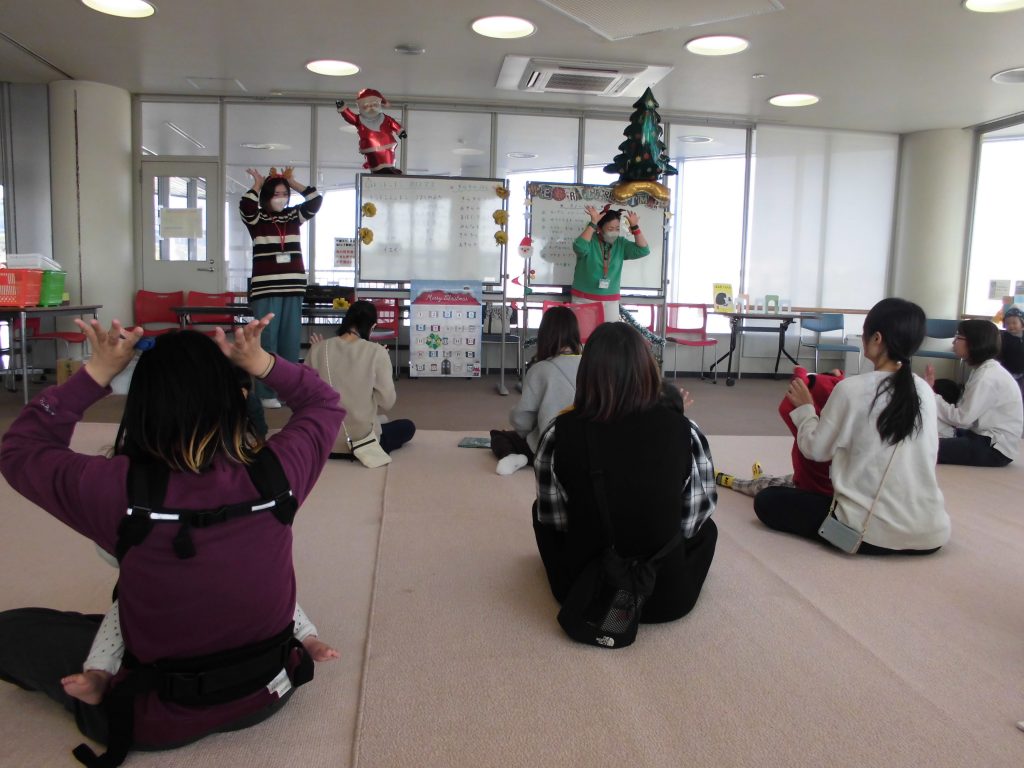 室内で活動している子供たちが、前方の大人の指導に従っている様子が写っている画像。