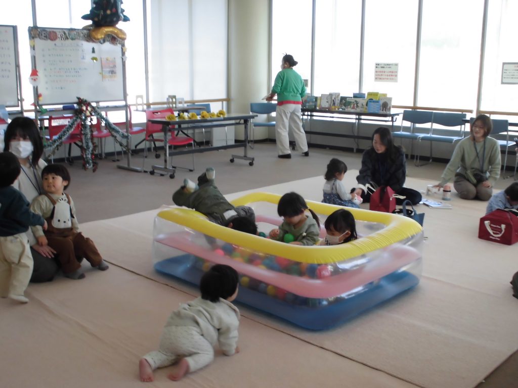 子供たちが遊んでいる室内の風景で、カラフルな遊具や大人が見守る様子が見られる。