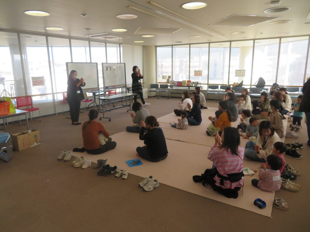 子供たちが床に座って活動している室内の様子が写っている画像です