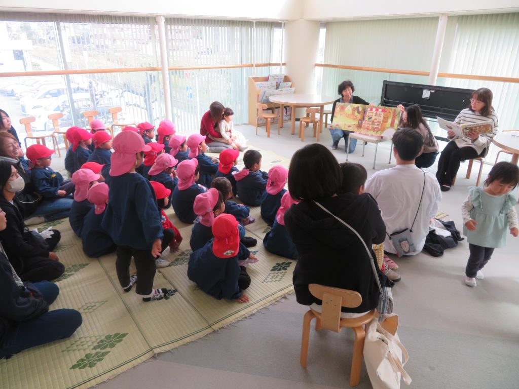 子供たちがピンクの帽子をかぶって座っている教室で大人たちが何かを行っている様子