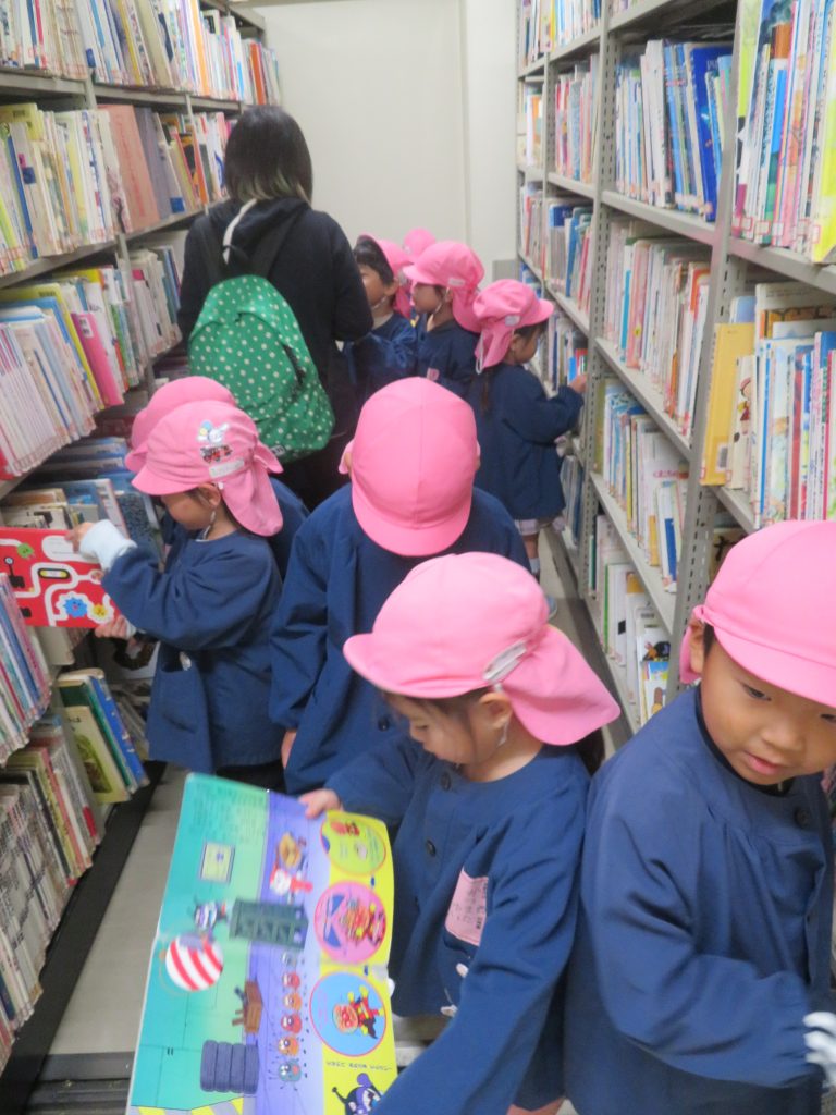 子供たちが図書館の本棚の前で本を見ている様子。