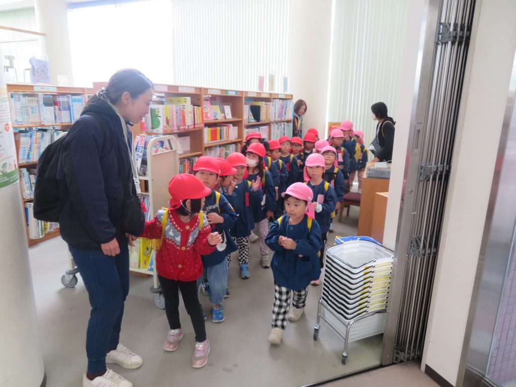 図書館内でオレンジ色の帽子をかぶった子どもたちが大人と一緒に活動している様子。