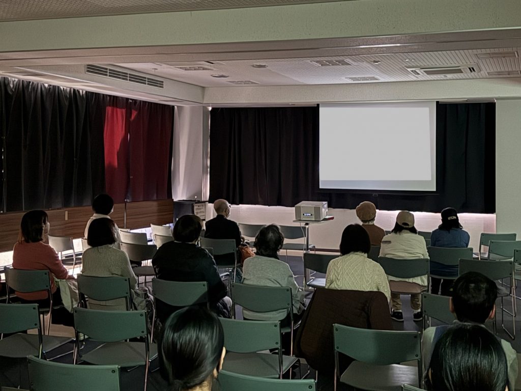 会議室でプレゼンテーションを受ける人々が椅子に座っている様子。