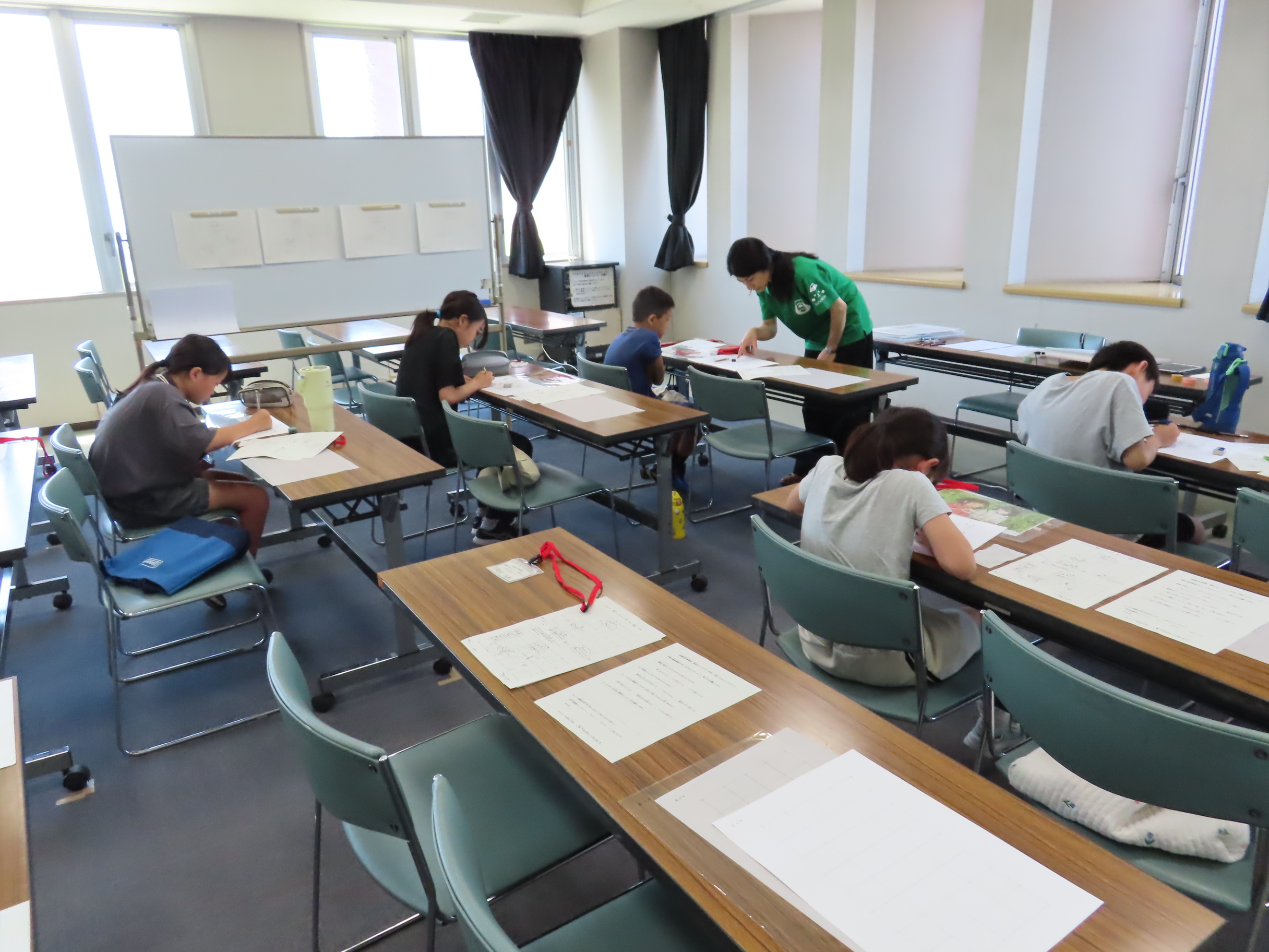 教室の机に向かいノートに書き込む子どもたちと一人の指導者が個別に教えている様子