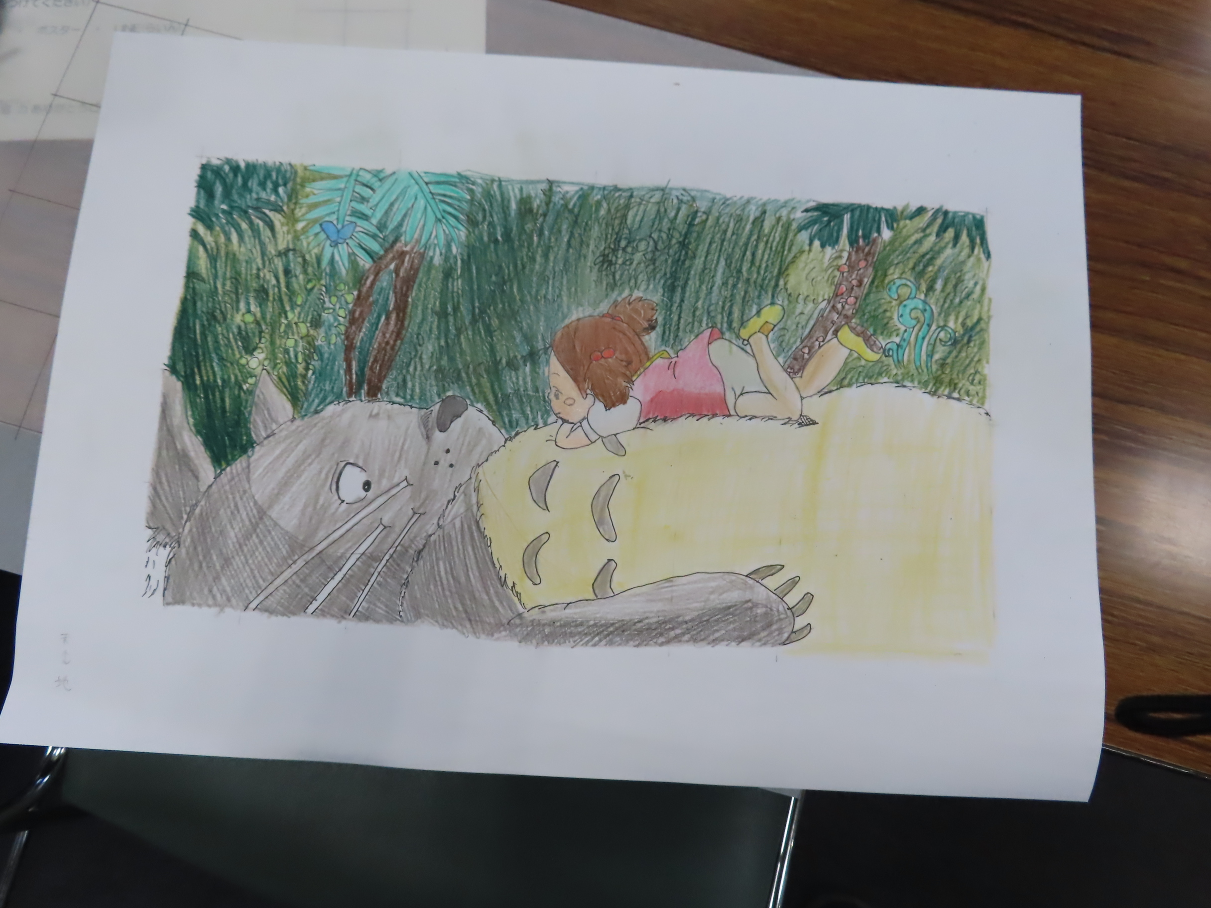 印刷された紙に大きな灰色のトトロの隣で小さな子どもが寝そべっているカラーの挿絵