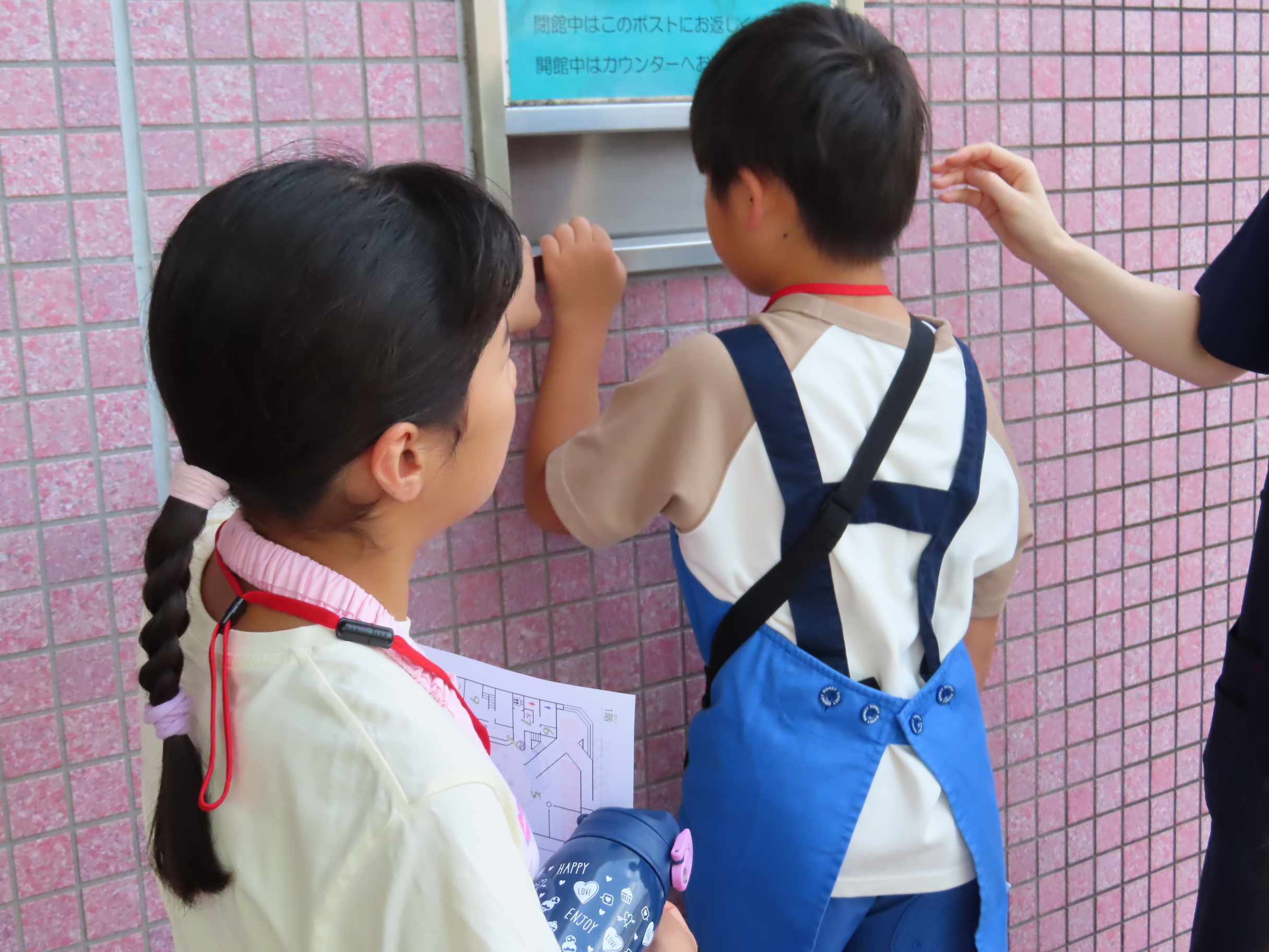 ブックポストを確認したりしている子ども二人とそばで手を差し伸べる大人