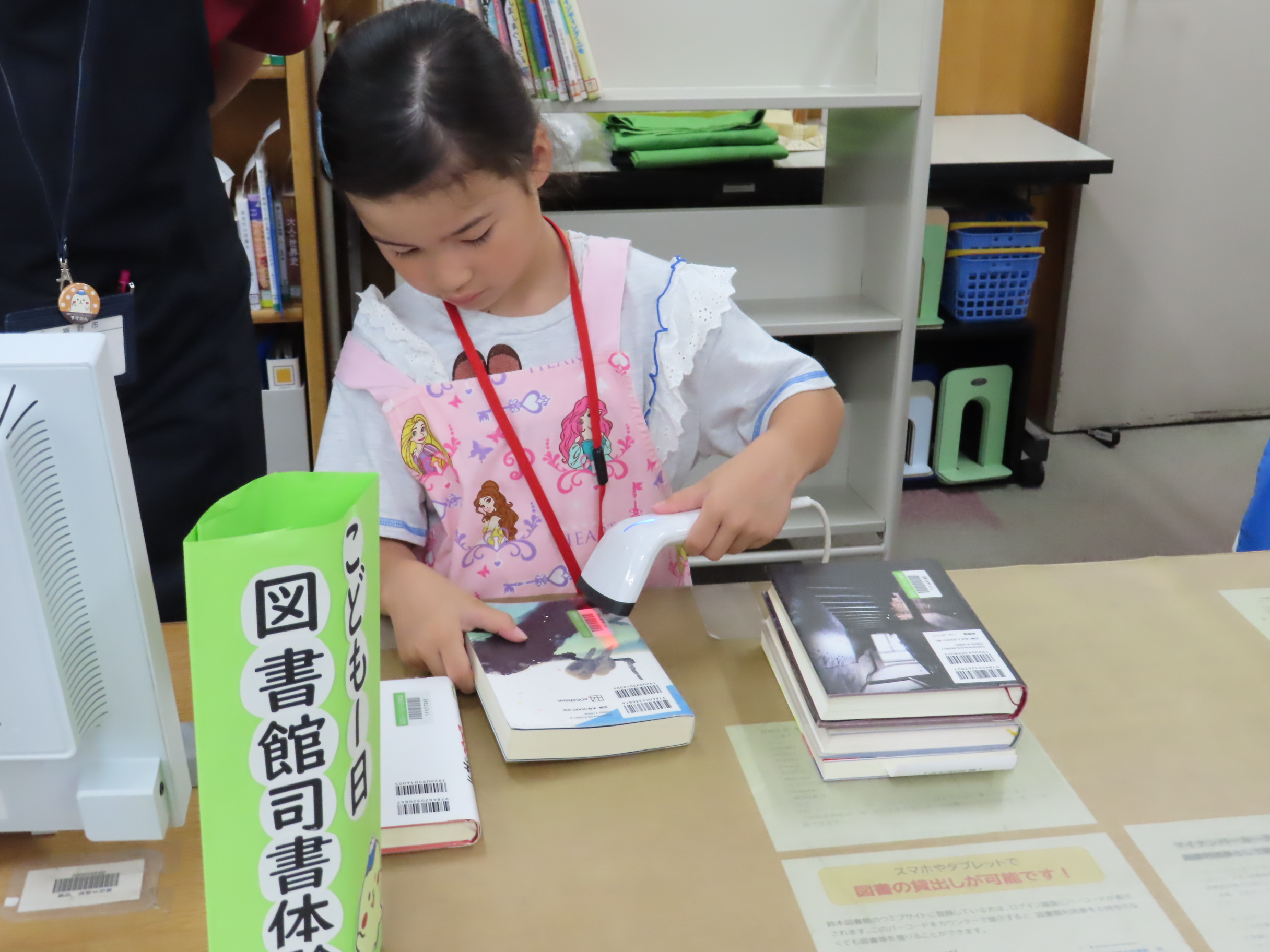 女の子が図書館のカウンターで本をバーコードリーダーで読み取り貸し出し手続きをしている