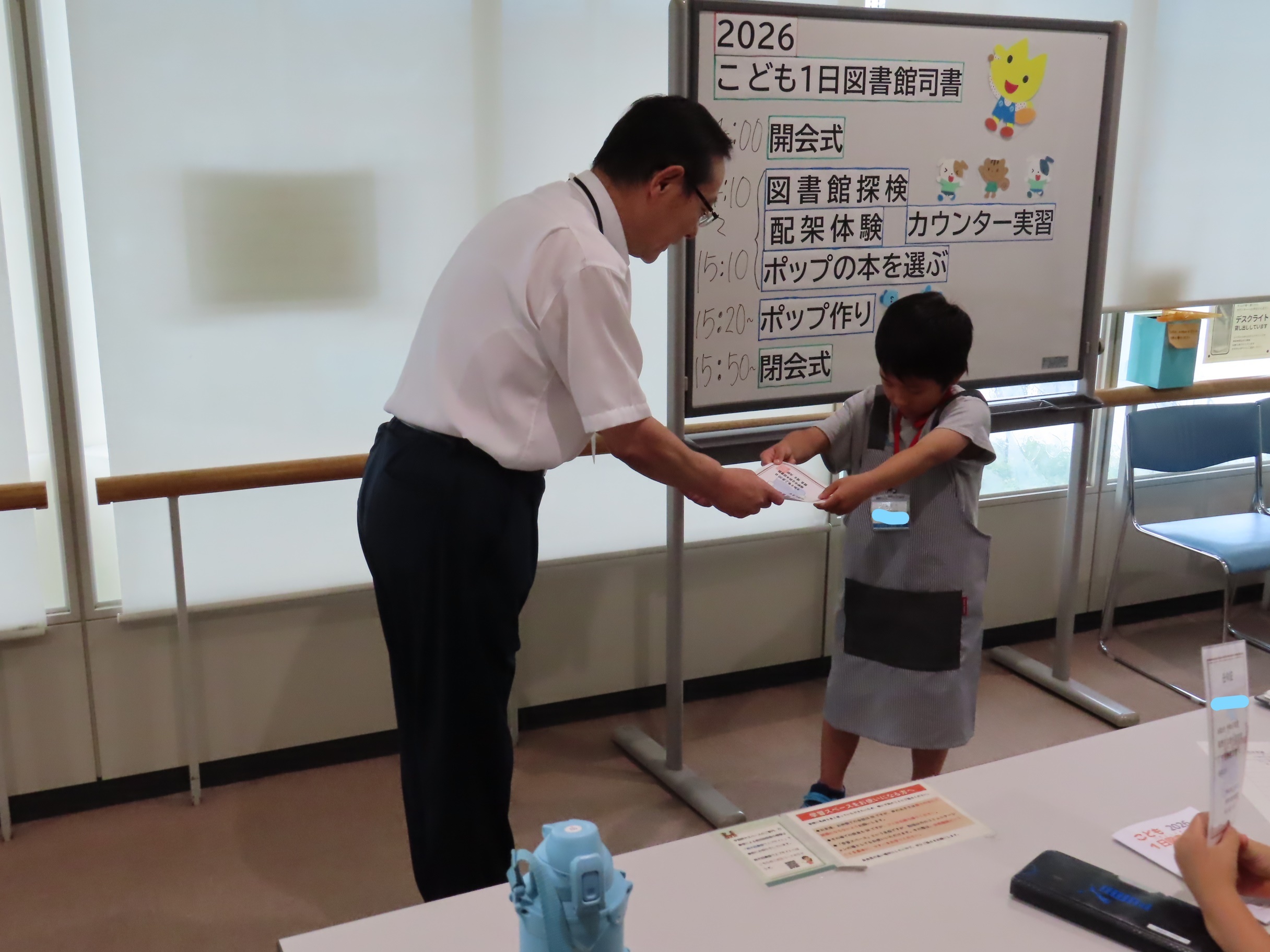 名札をつけた子どもに図書館長が両手で認定証を手渡している様子