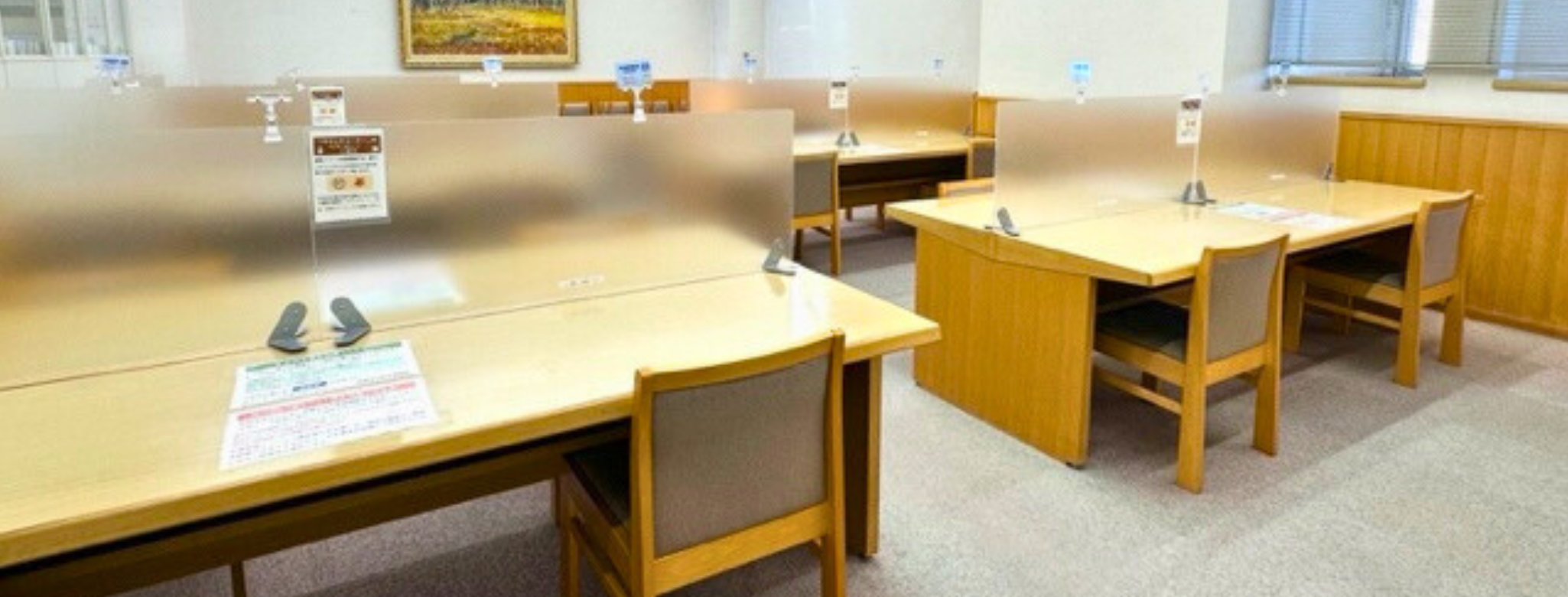 図書館の学習席が並ぶ木製の机と椅子が配置された静かな室内