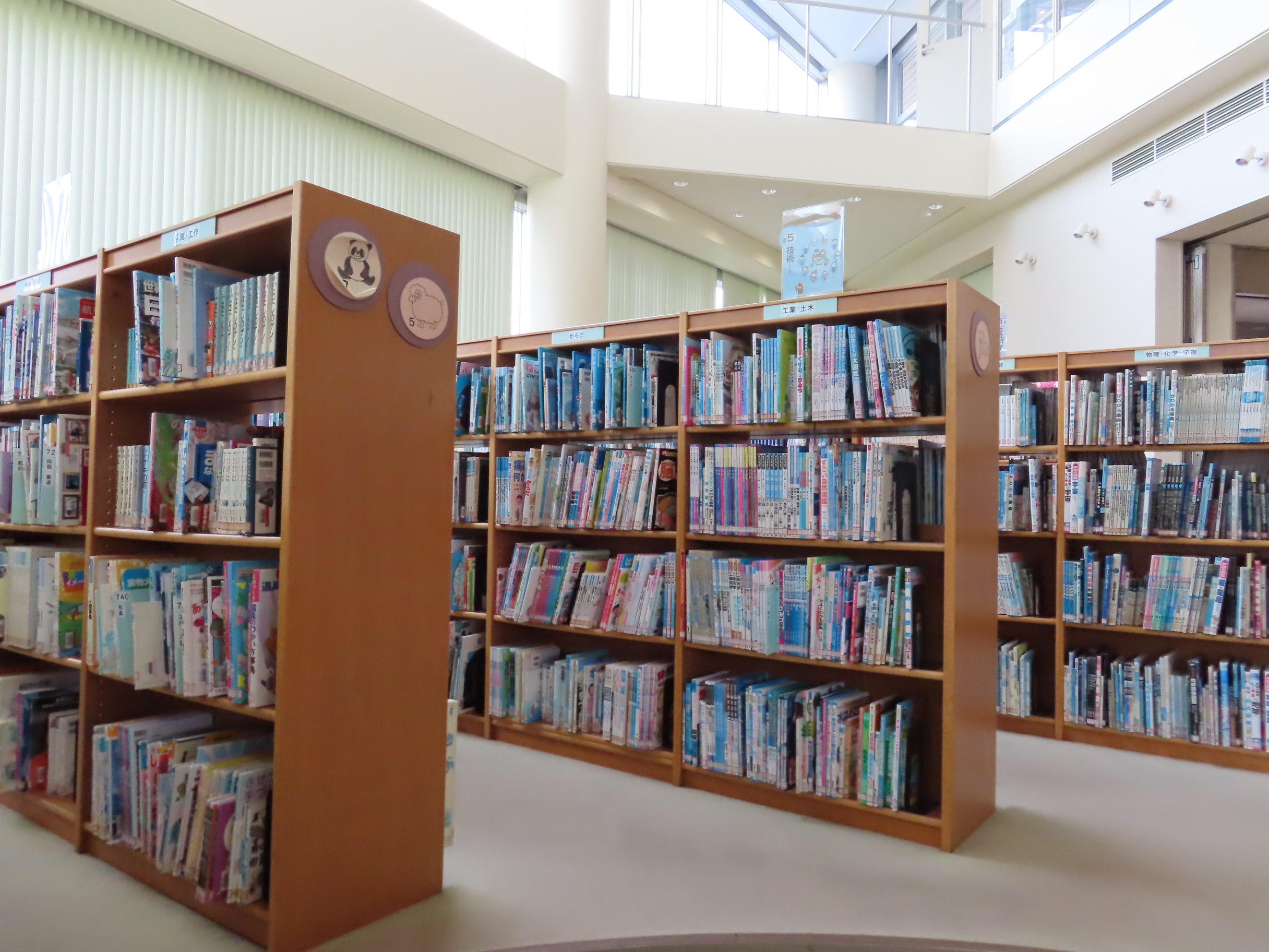 窓からの自然光が差し込む館内に木製の本棚が並び児童向けの本が整然と収められている