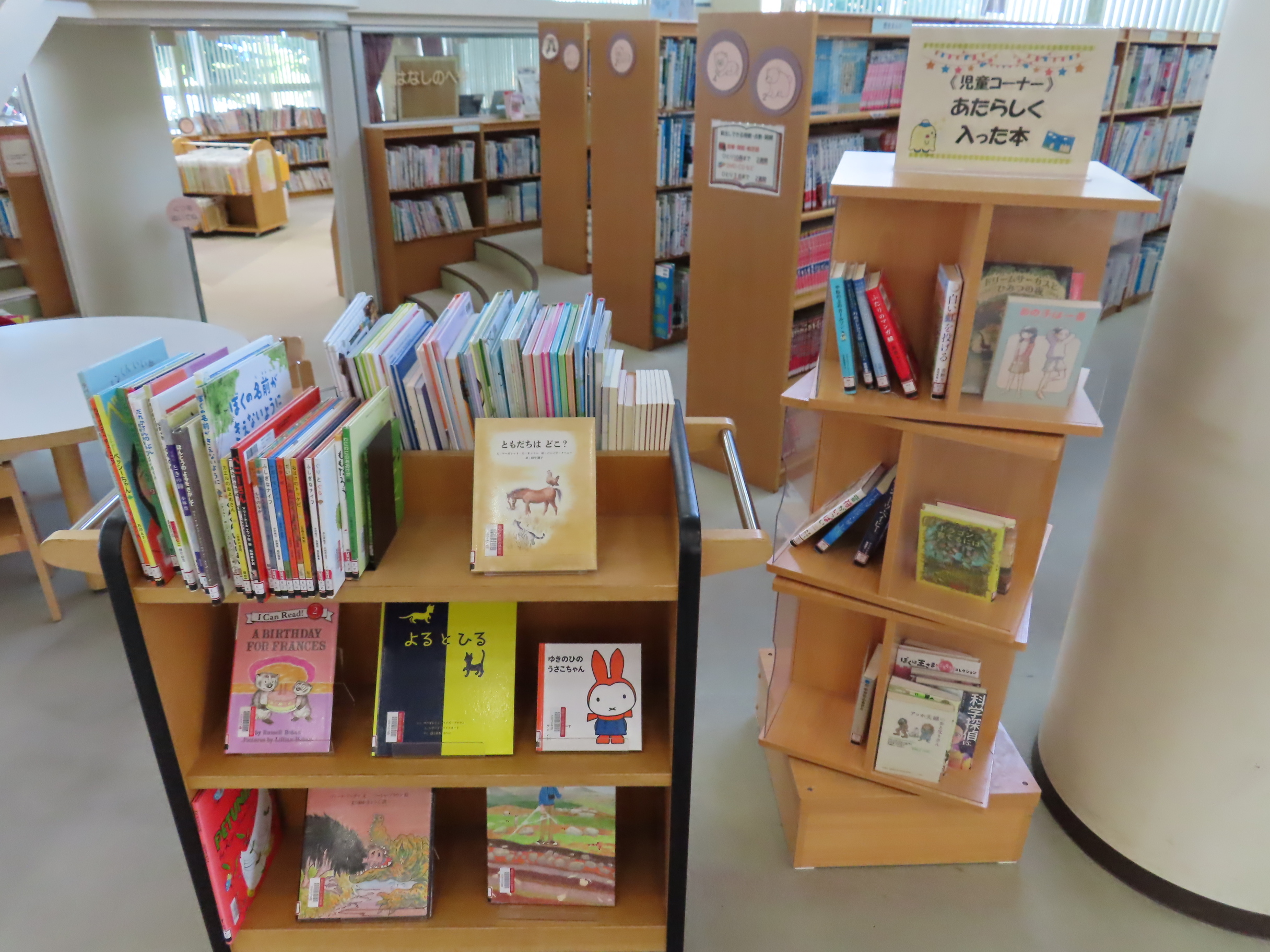 図書館の子ども向けコーナーに絵本が並んだ木製の棚があり新刊が並んでいる