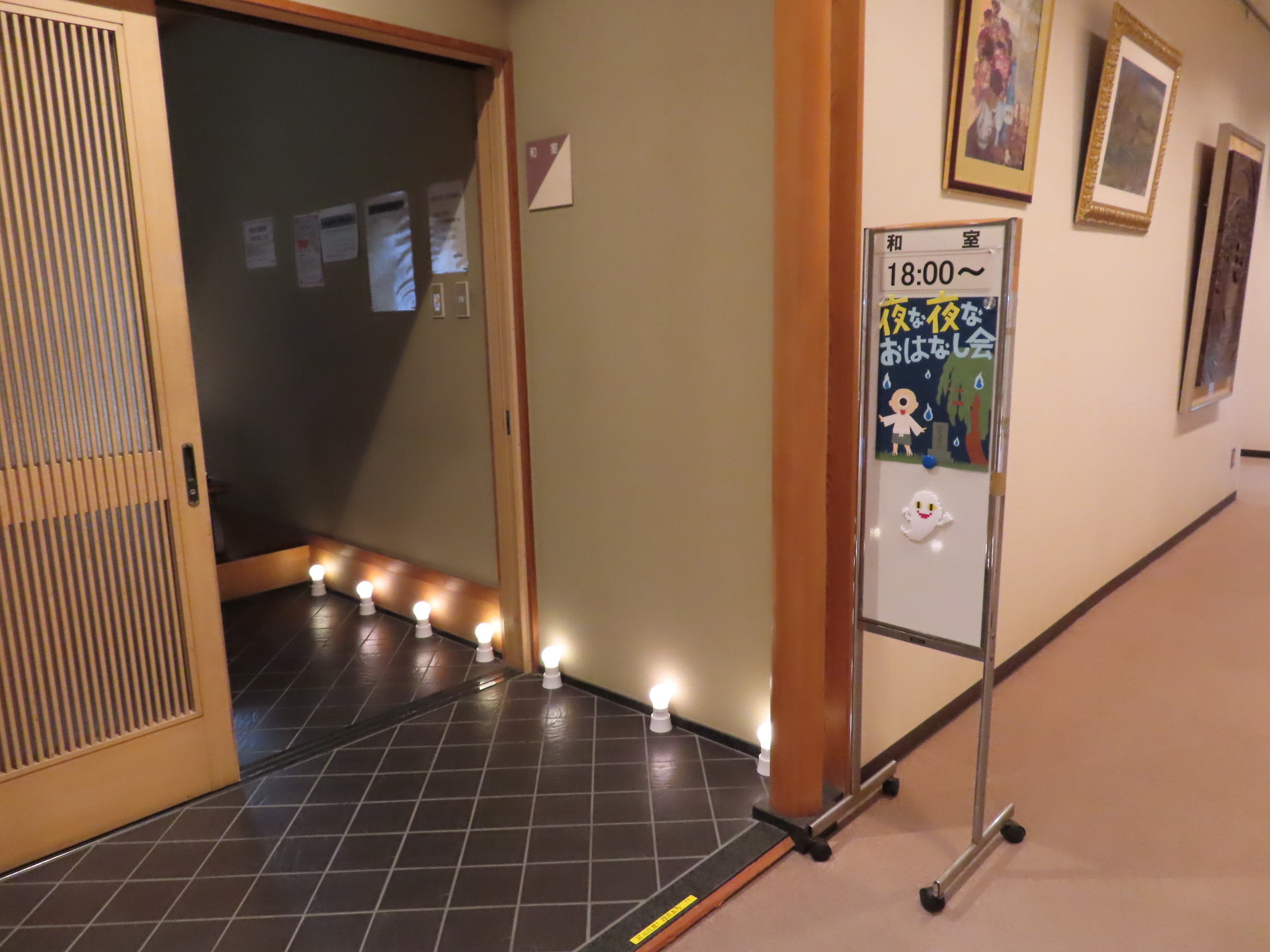 廊下の入口に障子風の引き戸と床に並べられた小さな灯りが置かれ案内看板にイベントの開始時刻が表示されている風景