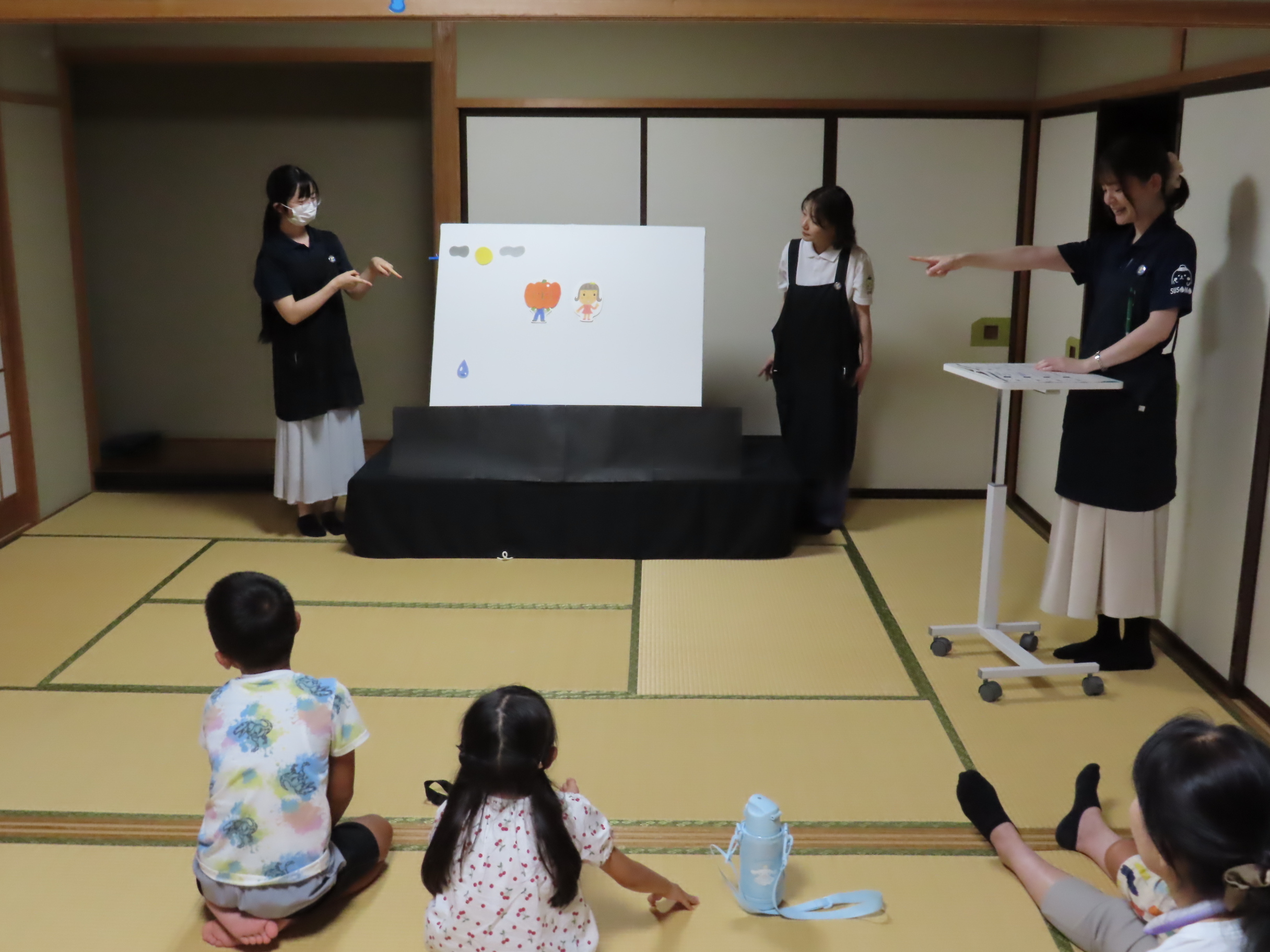 畳の部屋で床に座る子どもたちが前方のパネルシアターを見ている様子