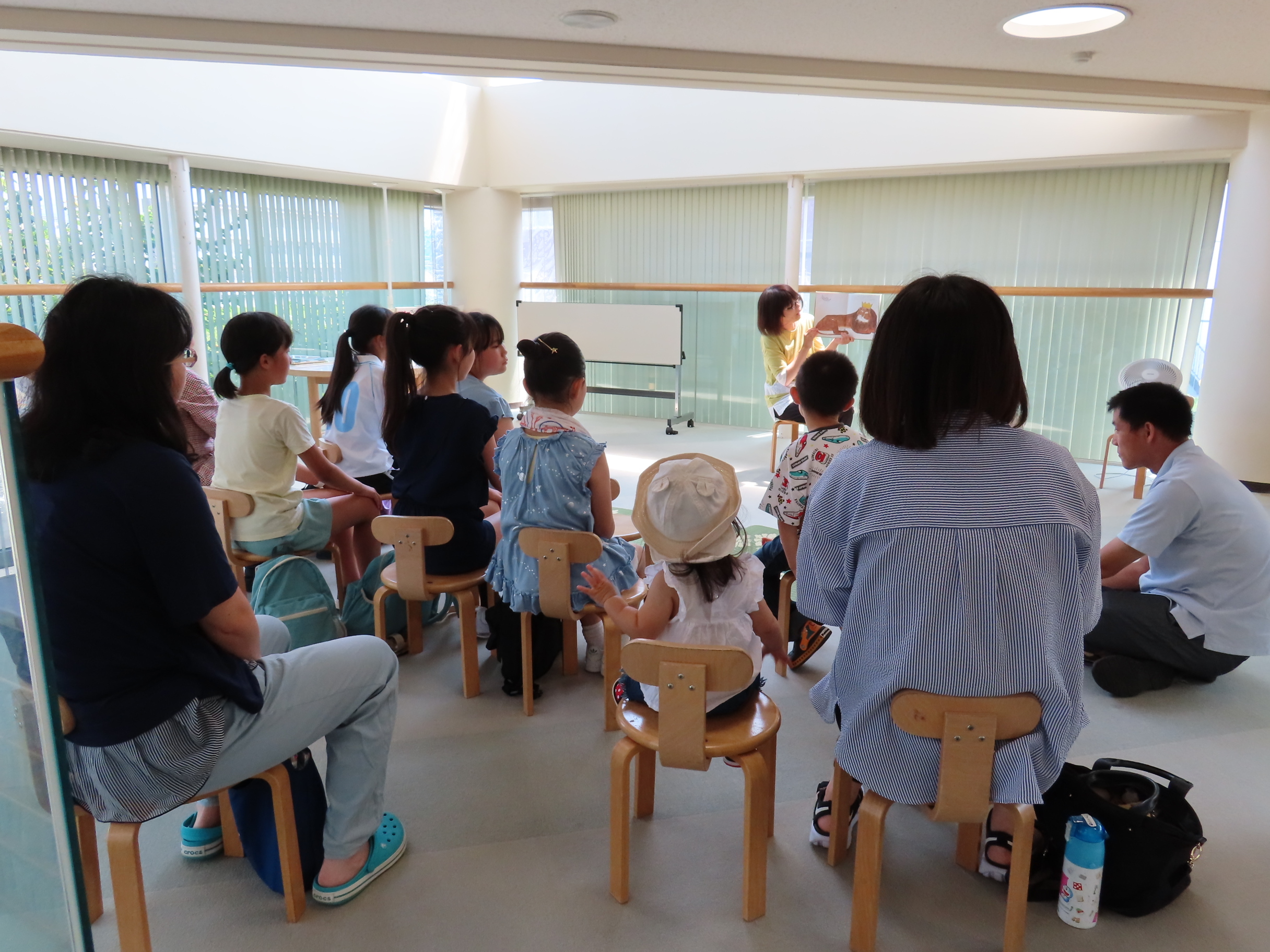 幼い子どもたちと大人が椅子に座り読み聞かせを聞いている様子