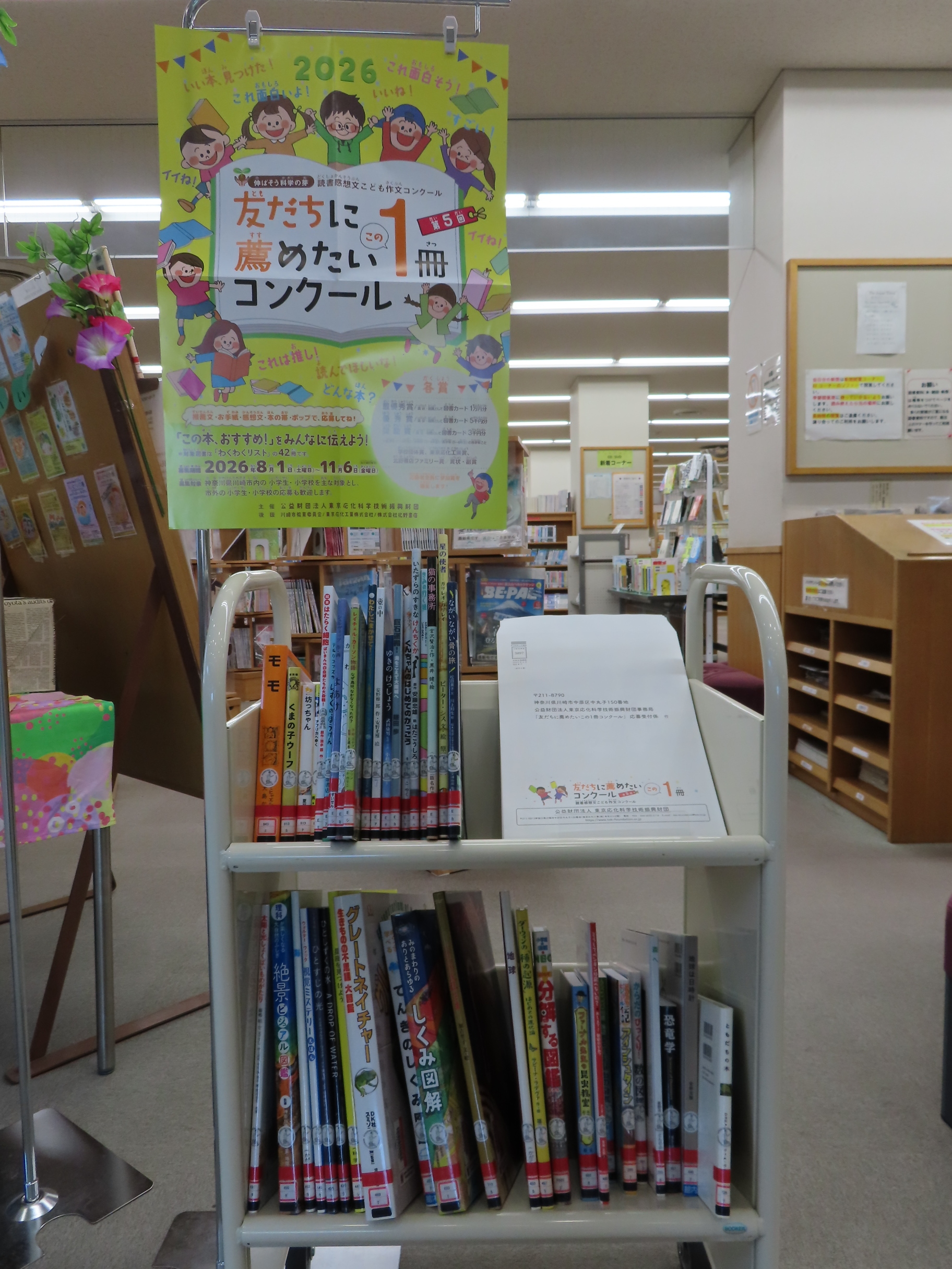 図書館のワゴン型の本棚に児童向けのポスターが掲示され絵本や児童書が並んでいる