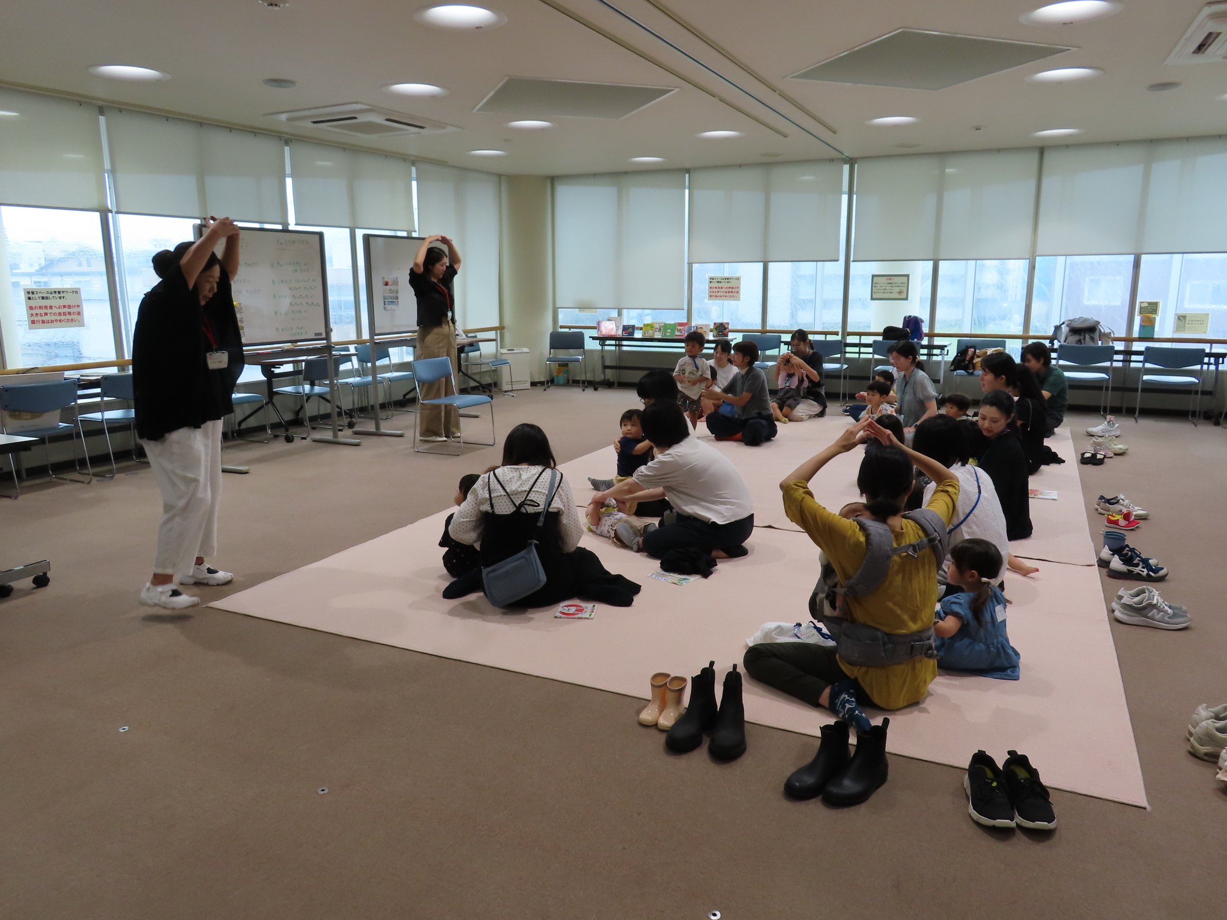 広い明るい室内で親子が手あそび「おおきなくりのきのしたで」をしている様子