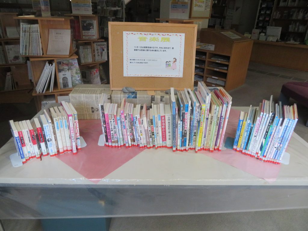 テーブルの上に並べられた色とりどりの本とその後ろに掲示されたサインがある図書館の風景。