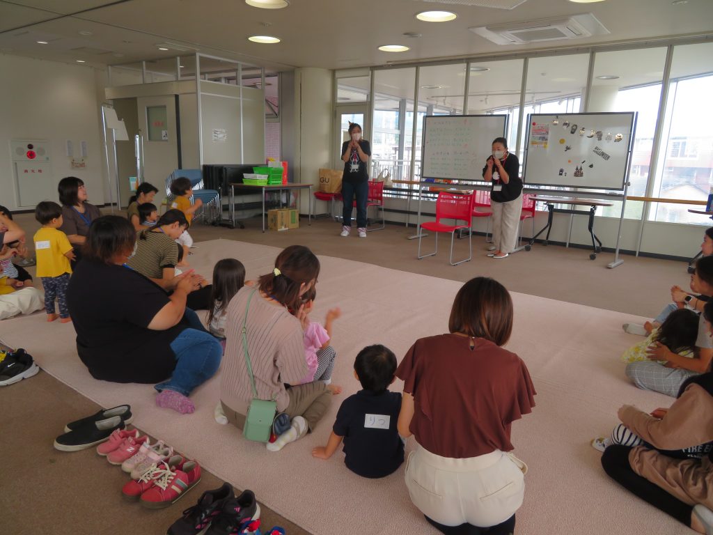 子供たちと大人が集まっている室内での活動の様子を描写した画像