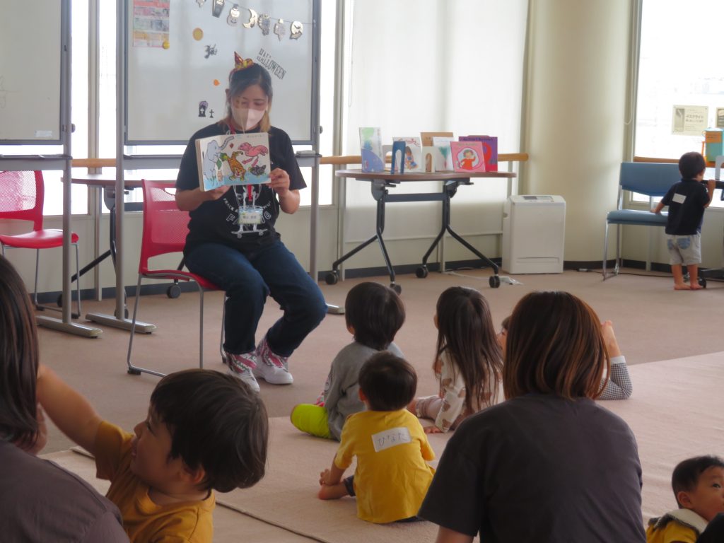 子供たちが座っている前で絵本を読み聞かせている大人の姿。