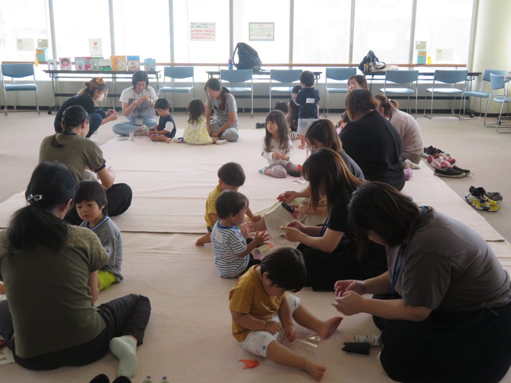 子供たちと大人が室内で遊んでいる様子を描いた画像。