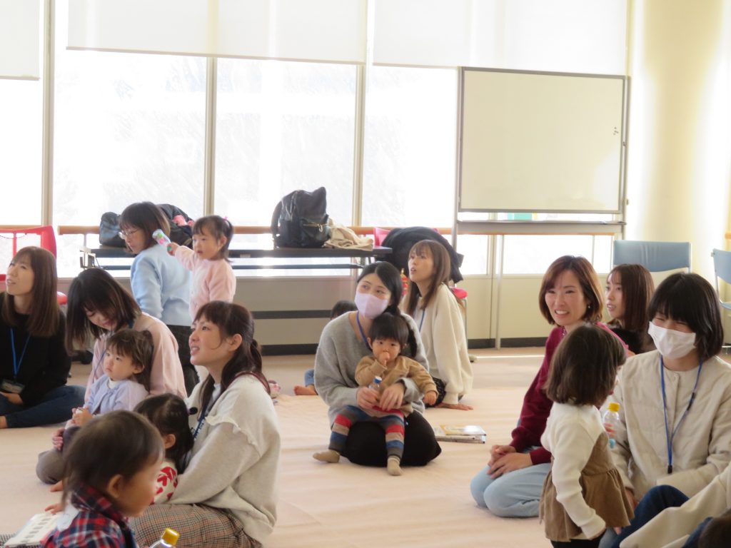 子供と大人が集まって座っている室内の様子。