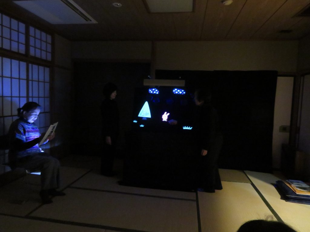 薄暗い部屋で光るスクリーンを見つめる人物が座っている画像です