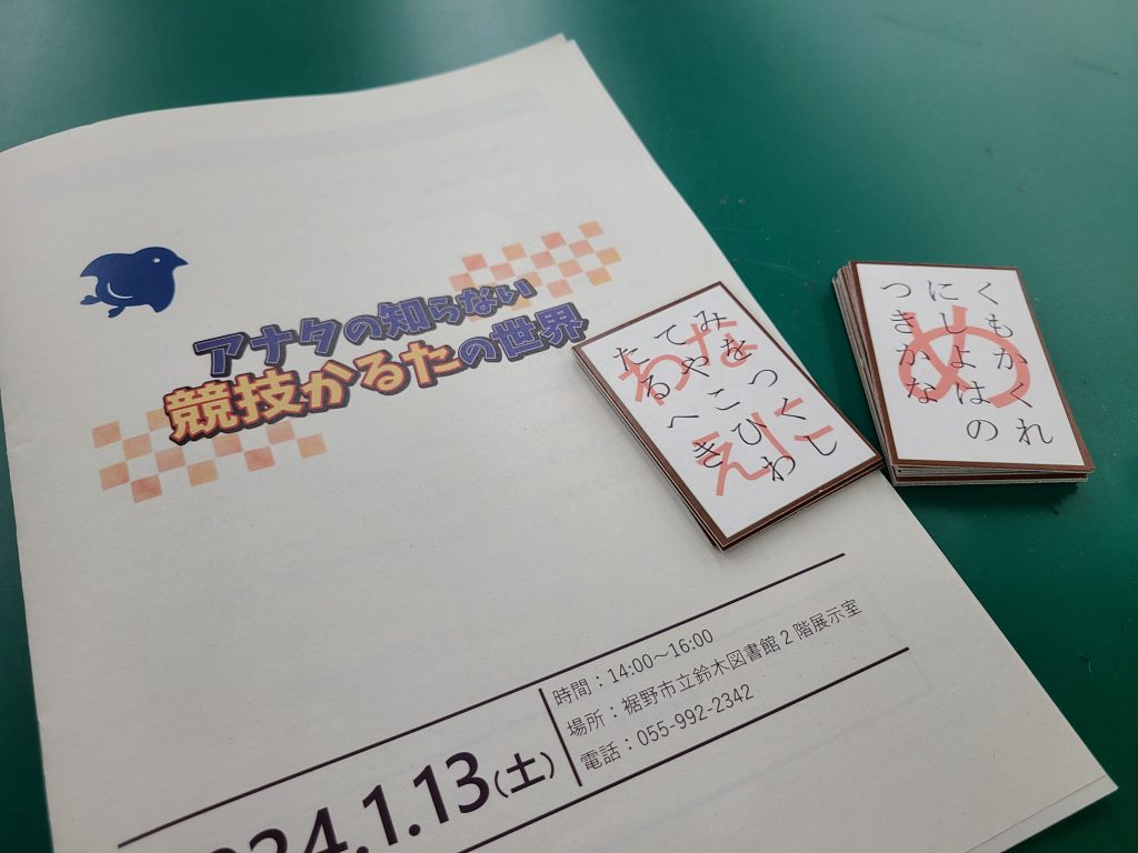 白い表紙の冊子と小さなカードが緑のテーブルの上に置かれている画像です