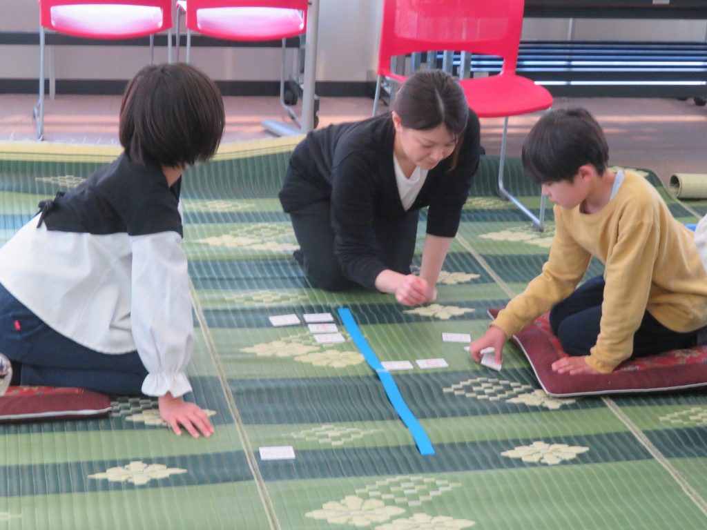子どもたちが床に座って遊んでいる様子で、カードを使って何かを学んでいる。