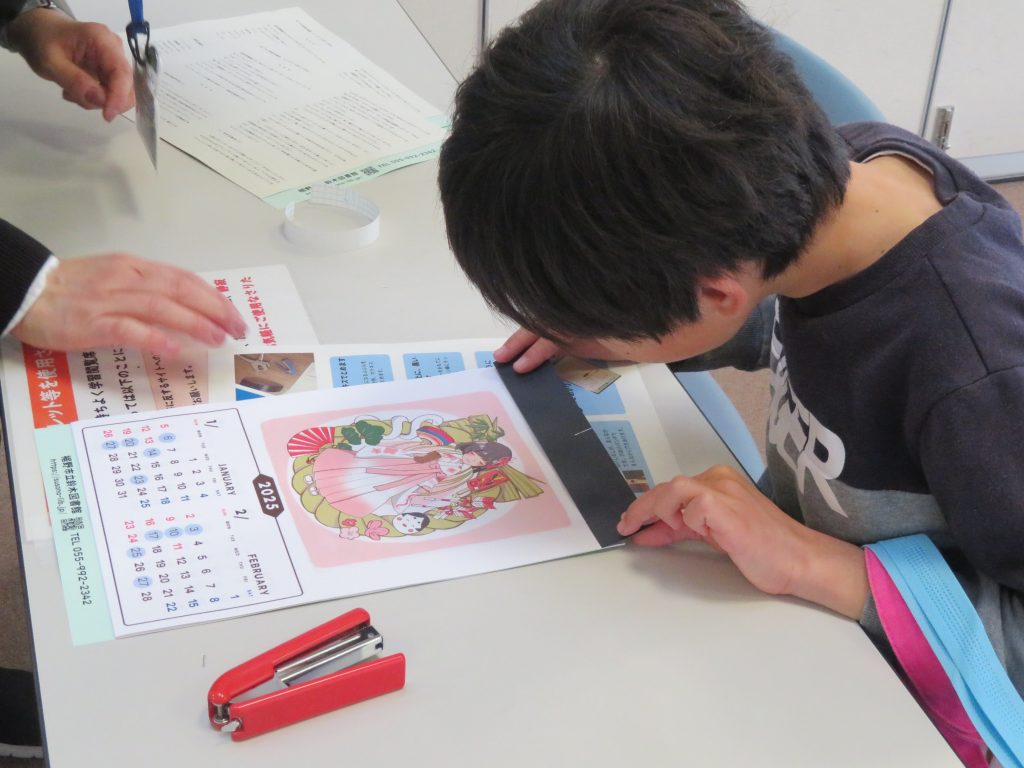 子供がテーブルにあるカレンダーやイラストを見ながら作業している様子。
