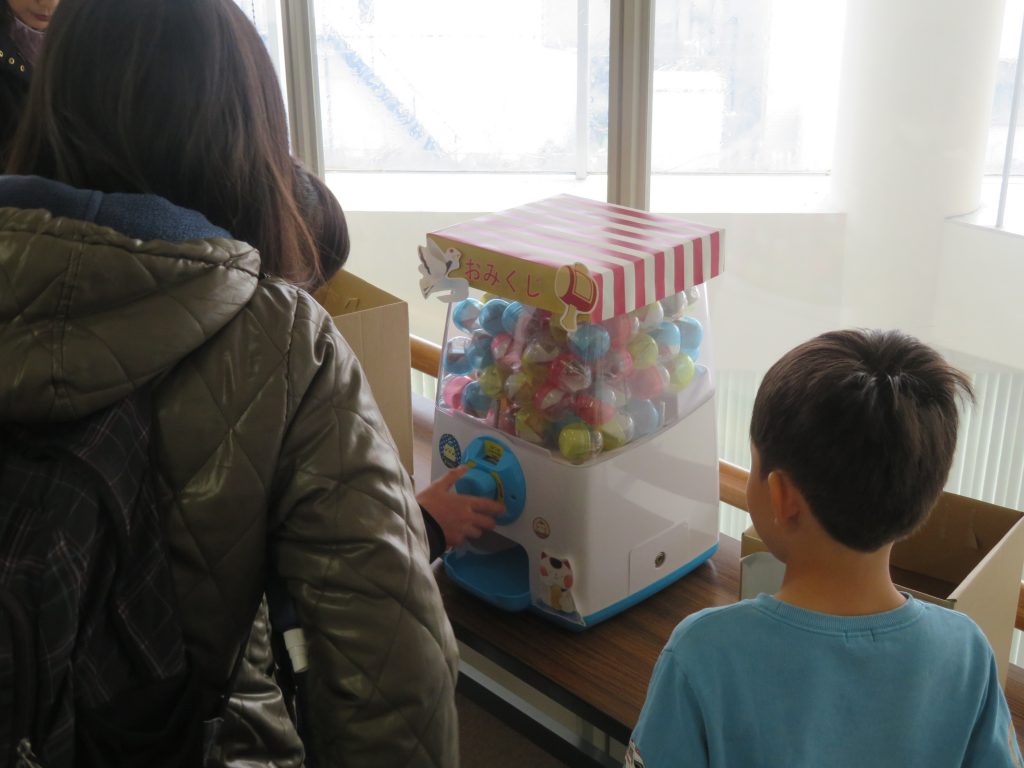 子供と大人がカプセル自動販売機の前に立っている様子。