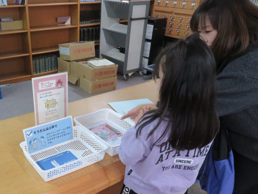 子供と大人がテーブルで何かを見ながら話し合っている図書館の風景。