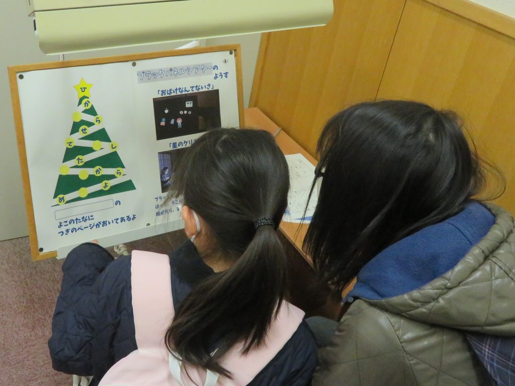 クリスマスツリーのポスターを見ている二人の子どもが写っている画像。