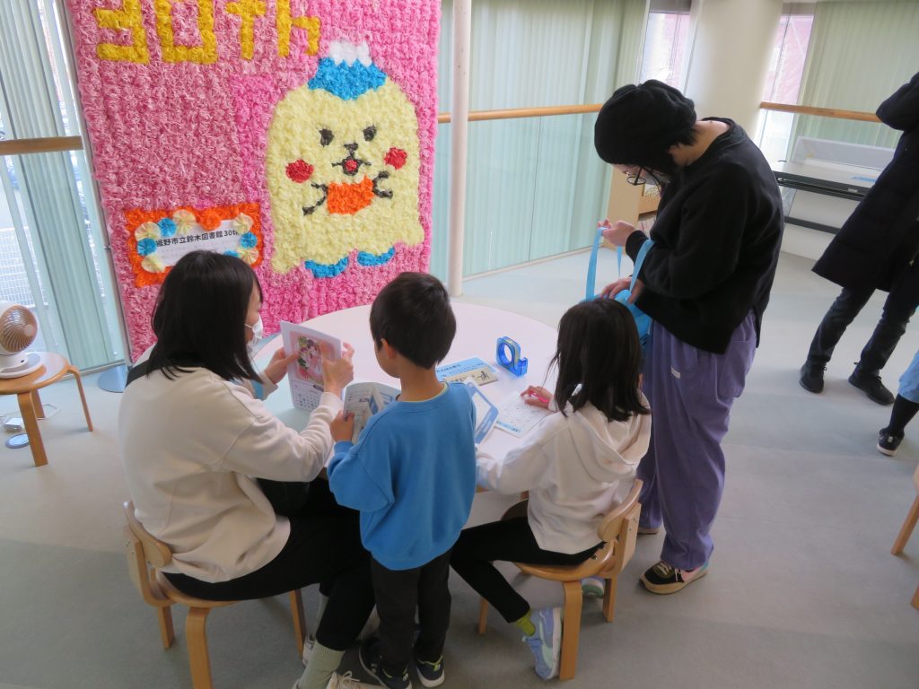 子供たちと大人がテーブルでアート活動をしている様子が描かれている。