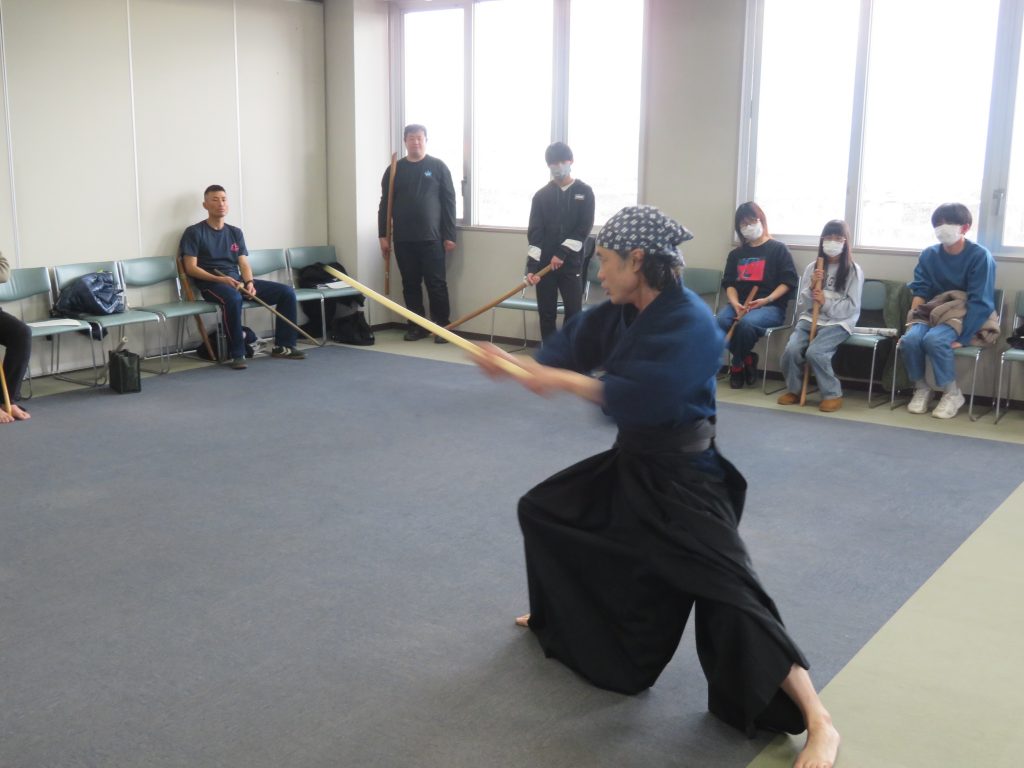 剣道の練習をしている人が、観客の前で竹刀を振っている様子。