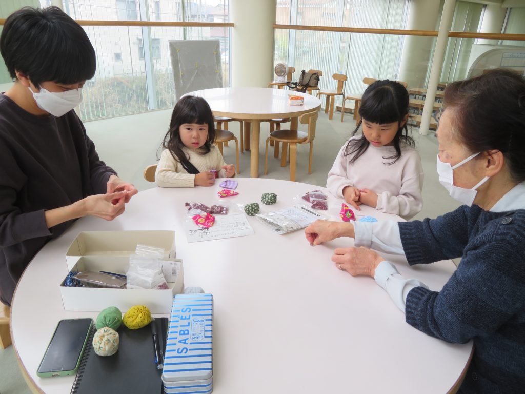 テーブルを囲んでいる大人と子供たちが何かを作成している様子を示す画像。