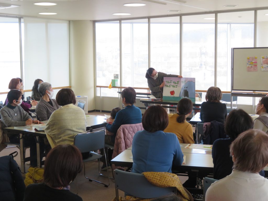 教室でプレゼンテーションを受ける人々が写っている画像。